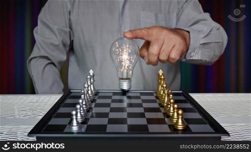worker touching light bulb on chess board with golden and silver chess pieces