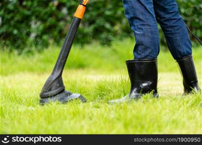 worker using a string lawn trimmer mower cutting grass at home