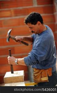 Worker using chisel and hammer on large block of wood