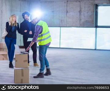 worker using laptop computer while showing house design plans to a young couple at construction site