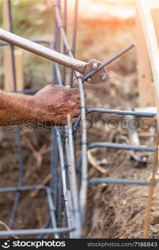 Worker Using Tools To Bend Steel Rebar At Construction Site.