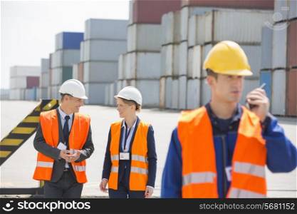 Worker using walkie-talkie while colleagues discussing in shipping yard