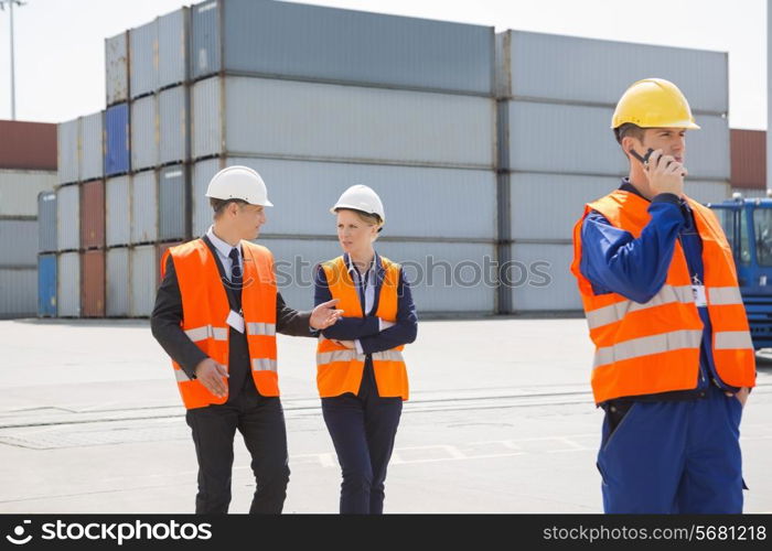 Worker using walkie-talkie while colleagues discussing in shipping yard