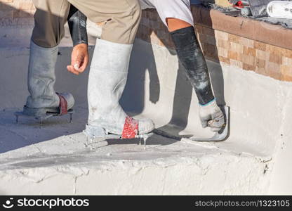 Worker Wearing Spiked Shoes Smoothing Wet Pool Plaster With Trowel.