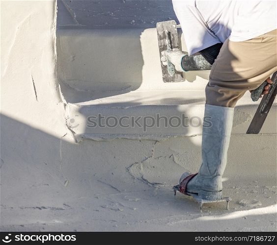 Worker Wearing Spiked Shoes Smoothing Wet Pool Plaster With Trowel.