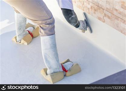 Worker Wearing Sponges On Shoes Smoothing Wet Pool Plaster With Trowel.