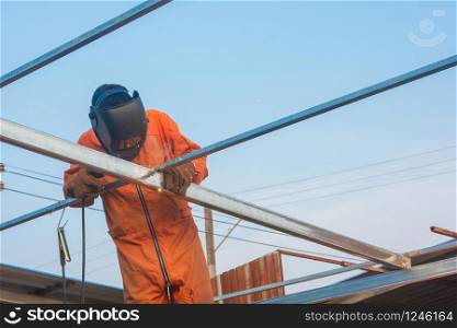 Worker welding in orange work clothes welding For roof truss