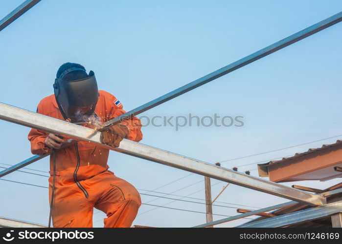 Worker welding in orange work clothes welding For roof truss