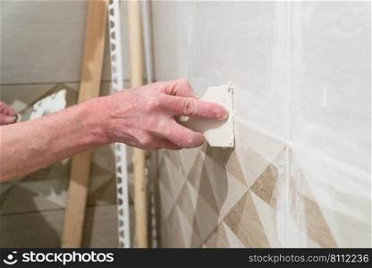 Worker with a rubber spatula fill the seams with a solution. Finishing works, blurred focus. The technology of laying tile.. Repair and finishing works