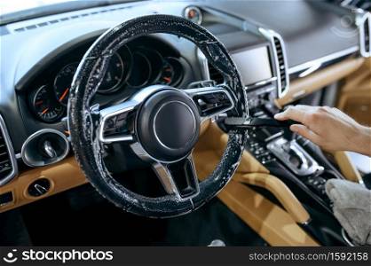 Worker with brush wipes car steering wheel, dry cleaning and detailing. Vehicle washing in garage, thoroughly care of automobile, chemical and clean service. Worker wipes car steering wheel, detailing