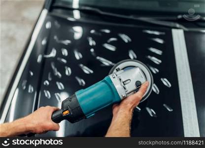 Worker with polishing machine cleans car hood. Auto detailing on carwash service. Worker with polishing machine cleans car hood