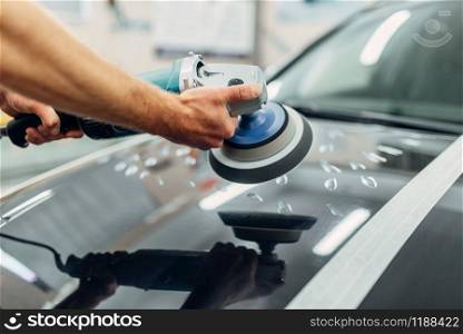 Worker with polishing machine cleans car hood. Auto detailing on carwash service