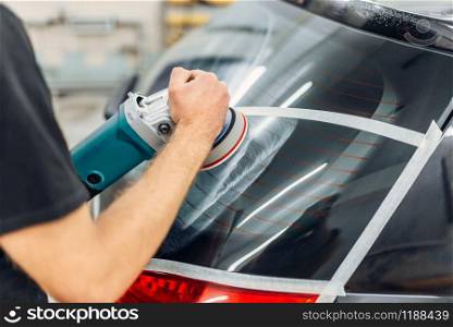 Worker with polishing machine removing the track from wiper blade on car window. Auto detailing on carwash service. Worker removes the track from wiper blade on car