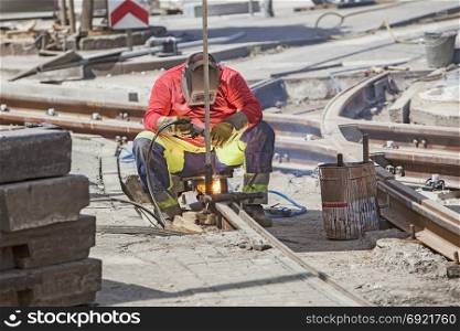 Worker with protective mask welding tram tracks in the city