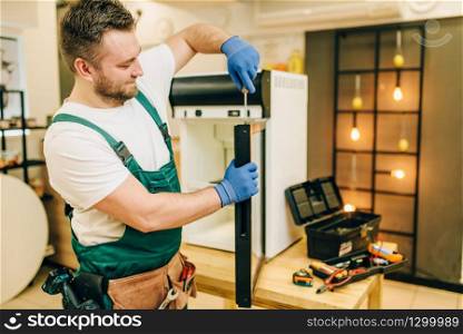 Worker with screwdriver repair refrigerator door at home. Repairing of fridge occupation, professional service. Worker with screwdriver repairs refrigerator door