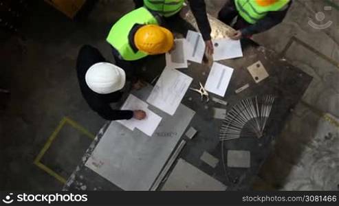 Workers and manager in safety helmets working with documents at factory