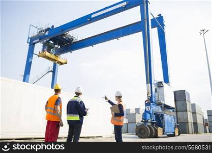 Workers discussing against large crane loading container at shipping yard