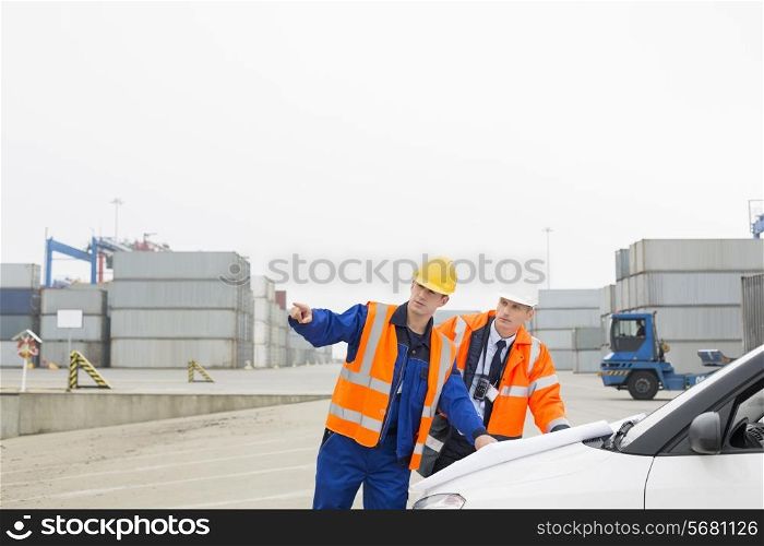 Workers discussing over blueprint in shipping yard