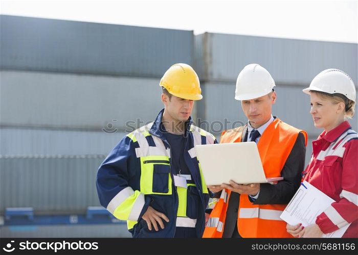 Workers discussing over laptop in shipping yard