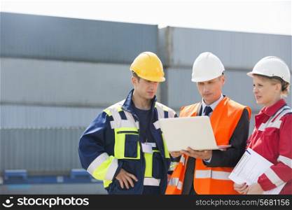 Workers discussing over laptop in shipping yard