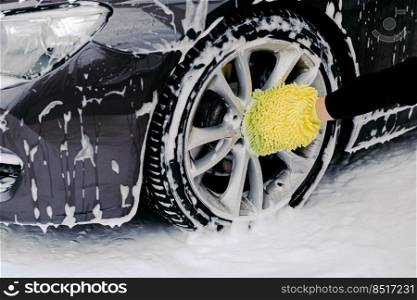 Workers hand with yellow sponge washing car wheels with detergent for cleaning vehicles. Maintenance and service concept