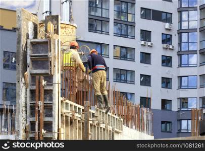 Workers poured concrete in the form work of the walls on the construction of the new house against the background of a modern residential building.. Workers poured concrete in the formwork of the wallsat a house construction