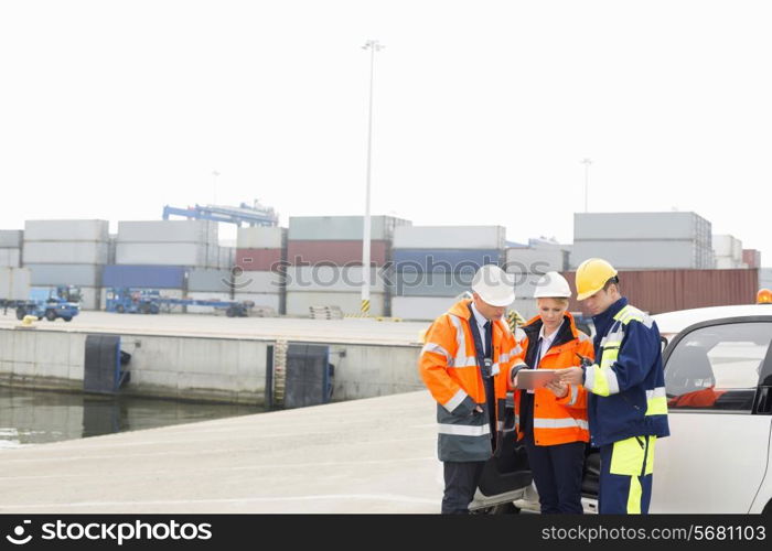 Workers using tablet PC beside car in shipping yard