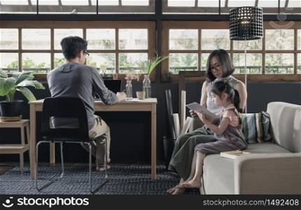 Working from home lifestyle father using laptop on the desk and child girl learning with her mother on sofa in the living room, Quarantine isolation during the Coronavirus (COVID-19) health crisis