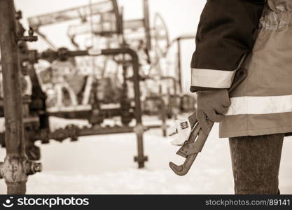 Working hand with wrenches on a wellhead crude oil site background. Toned sepia.