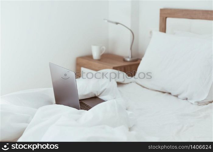Working home quarantine self isolation lockdown concept. Laptop in unmade bed. Comfortable and cozy remote home office. Modern apartments with sunlight and minimalistic design. Stay safe in pandemic.