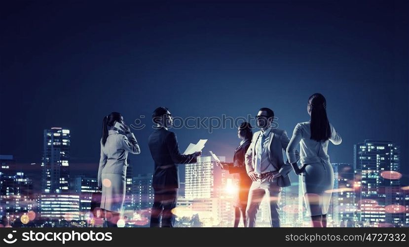 Working in cooperation. Group of business people in office against night city view