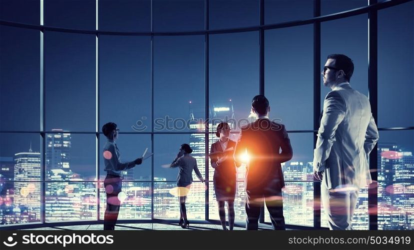 Working in cooperation. Group of business people in office against night city view