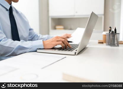 Working Man Conept The man sitting in front of the computer laptop at his desk, holding the document with his left hand and using his right hand holding a pen.