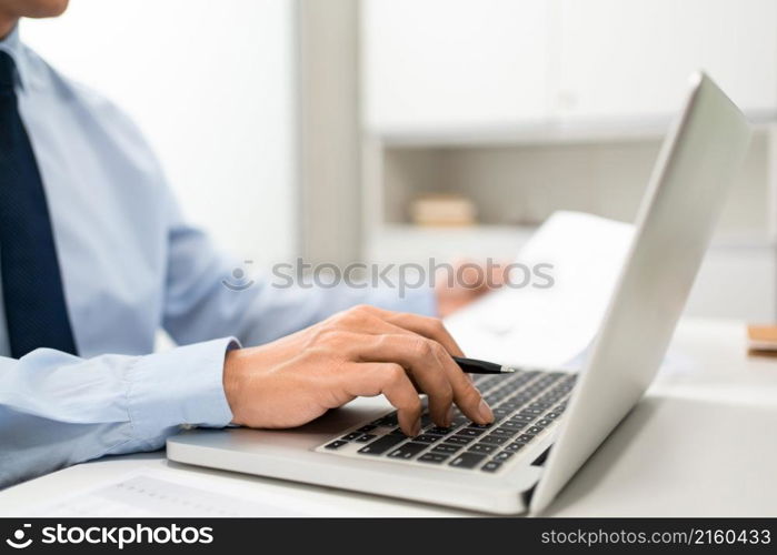 Working Man Conept The man sitting in front of the computer laptop at his desk, holding the document with his left hand and using his right hand holding a pen.