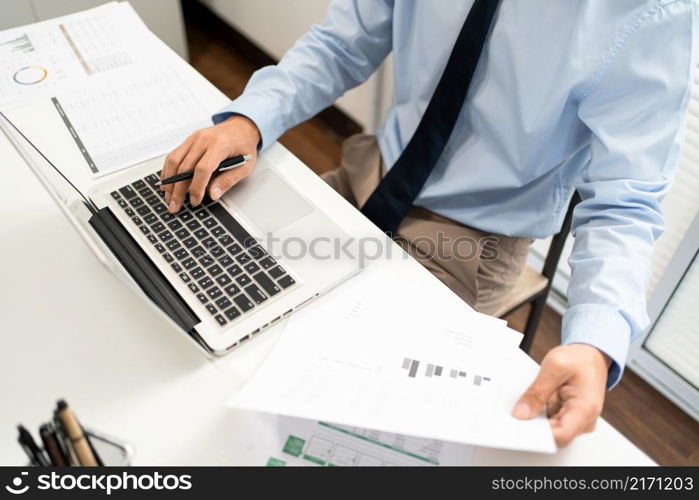 Working Man Conept The man sitting in front of the computer laptop at his desk, holding the document with his left hand and using his right hand holding a pen.