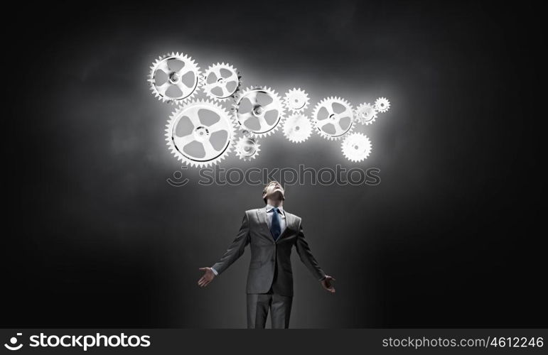 Working mechanism. Businessman with hands spread apart looking above at gears mechanism