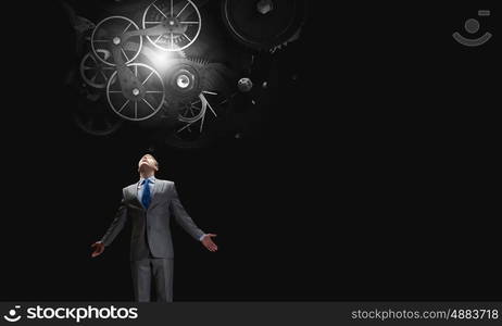 Working mechanism. Businessman with hands spread apart looking above at gears mechanism