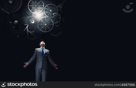 Working mechanism. Businessman with hands spread apart looking above at gears mechanism