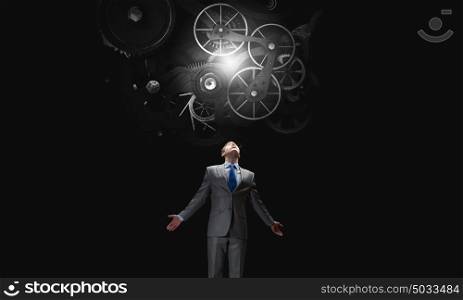 Working mechanism. Businessman with hands spread apart looking above at gears mechanism