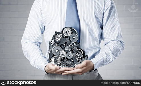 Working mechanism. Close up of businessman in suit holding metal gears in hands