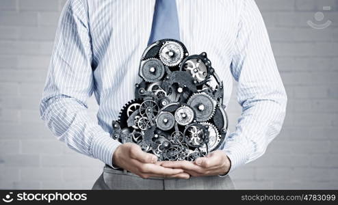 Working mechanism. Close up of businessman in suit holding metal gears in hands