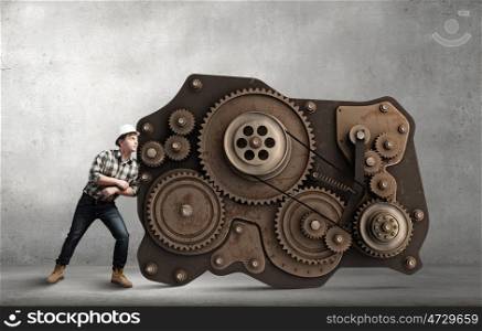 Working mechanism. Man builder trying to move big cogwheels mechanism