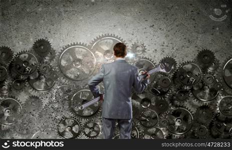 Working mechanism. Rear view of determined businessman with wrench in hands and cogwheels at background