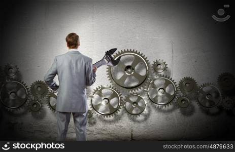 Working mechanism. Rear view of determined businessman with wrench in hands and cogwheels at background