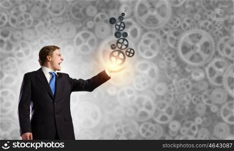 Working mechanism. Young anxious businessman holding gears in palm