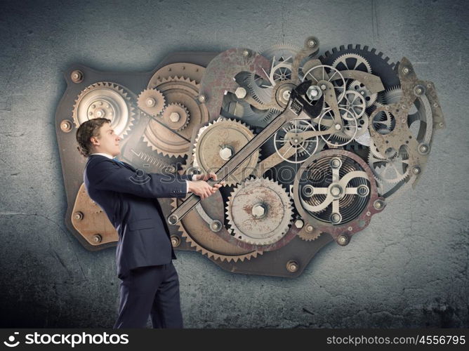 Working mechanism. Young businessman fixing gears mechanism with wrench