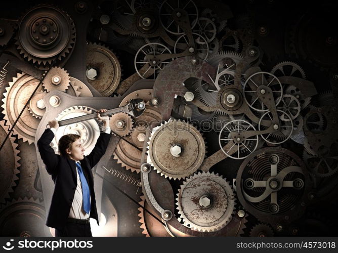 Working mechanism. Young businessman fixing gears mechanism with wrench