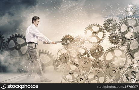 Working mechanism. Young businessman fixing gears mechanism with wrench