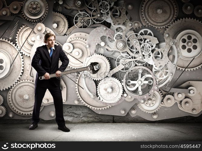 Working mechanism. Young businessman fixing gears mechanism with wrench