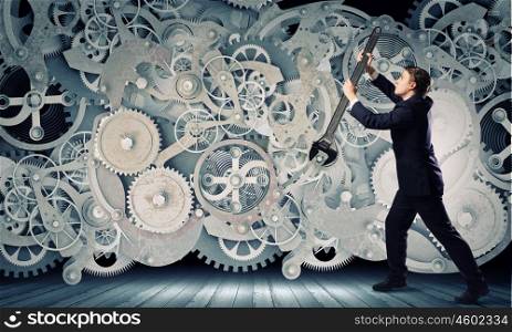 Working mechanism. Young businessman fixing gears mechanism with wrench